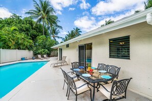 Ein Poolbereich mit Tisch und Stühlen, einer überdachten Terrasse und Blick auf einen Pool.