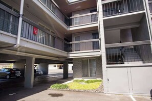 A multi-story building with balconies, a parking area, and a small garden. - NEW Downtown Hilo Bay Base for 31+ Night Stays (Hilo)
