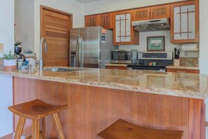 Eine Küche mit Holzausstattung, Edelstahlgeräten, Granit Arbeitsplatten und zwei Holzbarhocker.