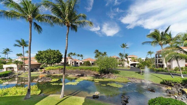 Un resort con fuente de agua, palmeras y edificios bajo un cielo azul claro.