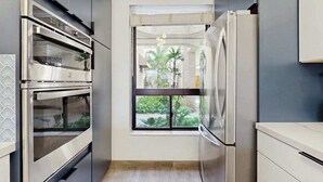 Una cocina moderna con electrodomésticos integrados, una ventana con vistas a zonas verdes y un diseño limpio y minimalista.