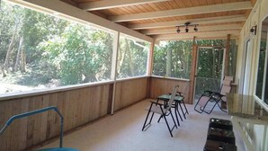 En inglasad veranda med träbjälkar, stora fönster och utsikt över skogen.