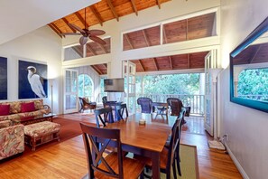 A spacious room with a high ceiling, wooden beams, a dining table with chairs, a sofa, and a television.