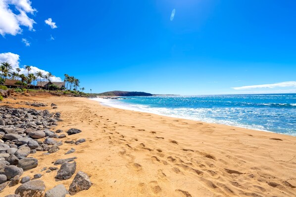 A beach with clear skies, a sandy shore, and scattered rocks.