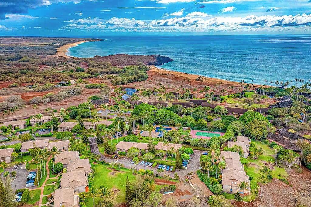 An aerial view of a coastal resort with multiple bungalow-style accommodations, a beach, and a clear view of the ocean.