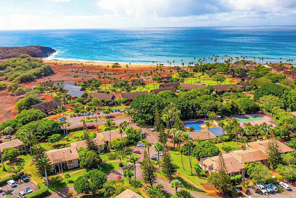 Oversigtsbillede af et resort med flere bygninger, en swimmingpool og en strand.