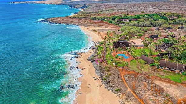 Vista aérea de uma área costeira com praia, piscina e vários edifícios.