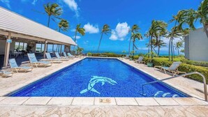 A swimming pool with a dolphin logo, lounge chairs, and a view of the ocean. - *New* Fall Sale Two-Bedroom Molokai Stay with Balconies and Pool (Kaunakakai)