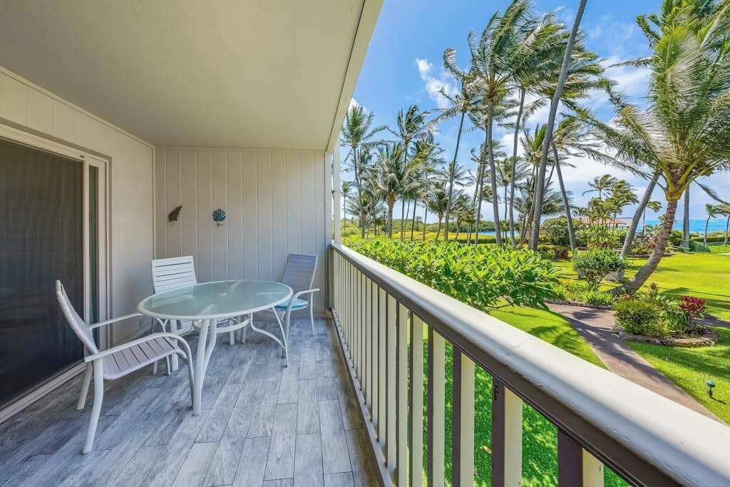 A balcony with a table and chairs, a view of palm trees, and a well-maintained lawn.