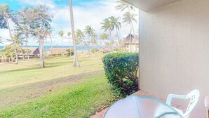 A balcony with a view of a grassy area, palm trees, and a building in the distance. - New Fall Sale Ocean View Studio Near Kepuhi Beach and Sunset Pool (Maunaloa)