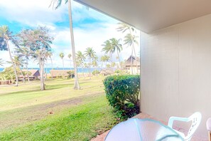 A room with a view of a grassy area, palm trees, and a building in the distance.