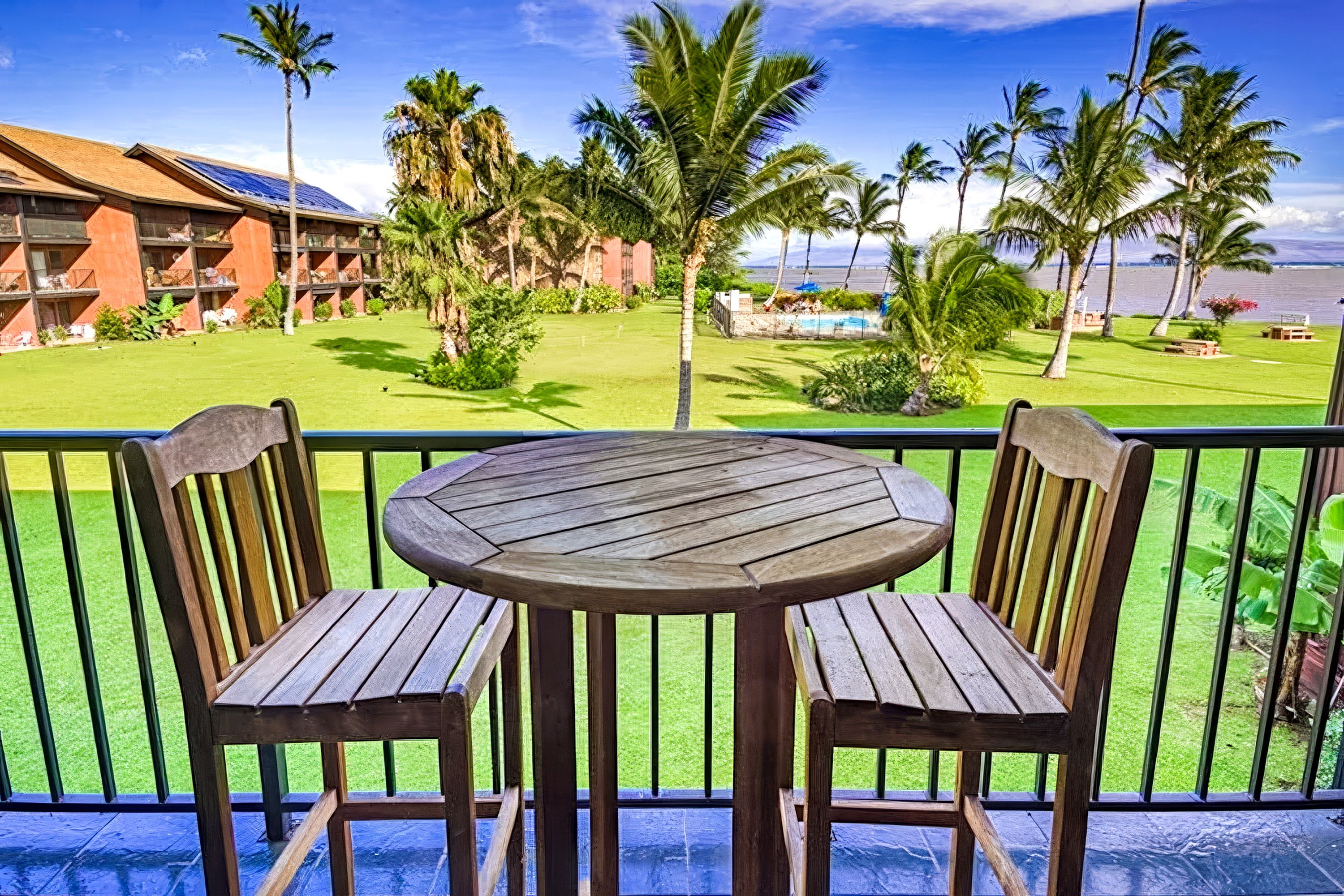Ein Holztisch und Stühle auf einem Balkon mit Blick auf einen Pool und Palmen.