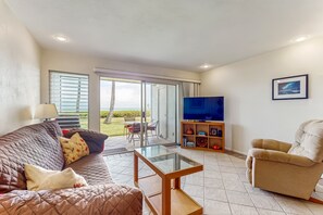 Una sala de estar con un sofá, una mesa de centro de vidrio, un televisor sobre un mueble de madera y una silla.