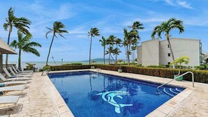 Ein Pool mit Liegestühlen, Palmen und einem Gebäude im Hintergrund.