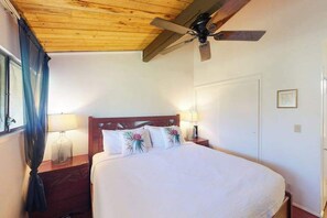 Ein Schlafzimmer mit Holzbalkendecke, einem Bett mit weißer Bettwäsche, zwei Nachttischlampen und einem Deckenventilator.