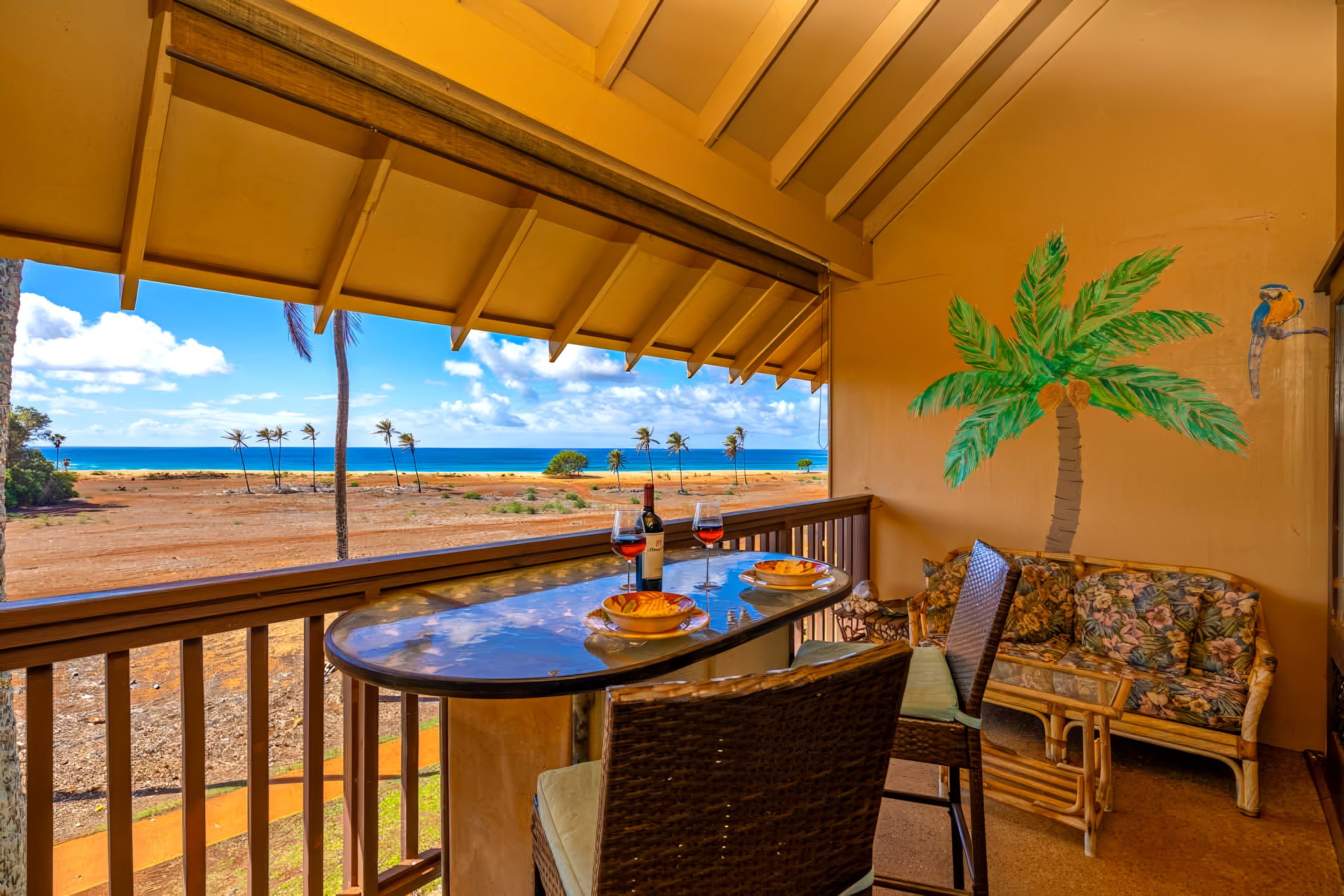Un balcón con mesa y sillas, con vista a una playa con palmeras y el océano.