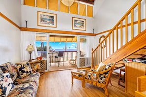 A spacious living area with a wooden staircase, a balcony with a view, and a dining area with outdoor seating.