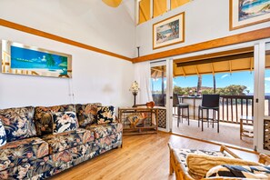 A living room with a sofa, a table with a guitar, and a view of the outdoors through a sliding door.