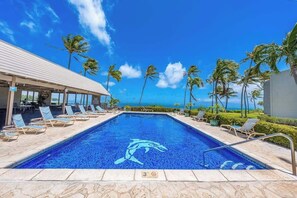 A swimming pool with a dolphin design, surrounded by lounge chairs and palm trees, with a view of the ocean. - *NEW* Third-Floor Molokai Oceanfront Views with Pool (Kaunakakai)
