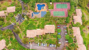 An aerial view of a resort with a swimming pool, tennis courts, and a parking area surrounded by greenery. - *New* Fall Sale Molokai Two-Bedroom Retreat by Kepuhi Beach (Maunaloa)