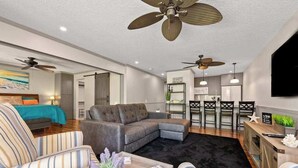 A modern living room with a sectional sofa, a coffee table with a plant, a dining area with chairs, and a kitchen in the background. - *New* Fall Sale Molokai Two-Bedroom Retreat by Kepuhi Beach (Maunaloa)
