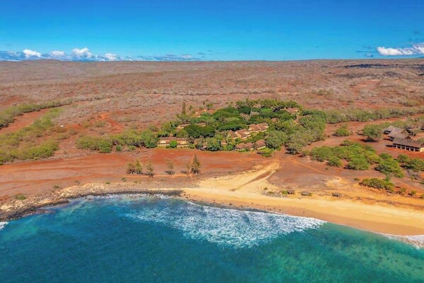 A coastal landscape with a beach, clear blue waters, and a small cluster of buildings surrounded by sparse vegetation. - NEW Fall Sale Colorful Molokai Condo Near Kepuhi Beach with Lanai and Pool (Maunaloa)