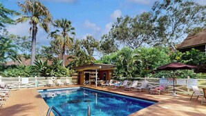 Piscina com espreguiçadeiras e um pequeno pavilhão.