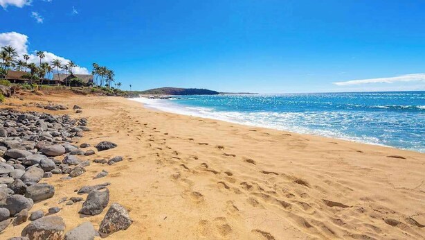Uma praia com águas azul-claras, uma costa arenosa e uma montanha ao longe.