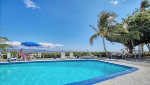 A swimming pool with lounge chairs and umbrellas, surrounded by palm trees and a clear sky. - *New* Fall Sale Molokai Studio for Poolside Sunsets Near Kaunakakai (Kaunakakai)