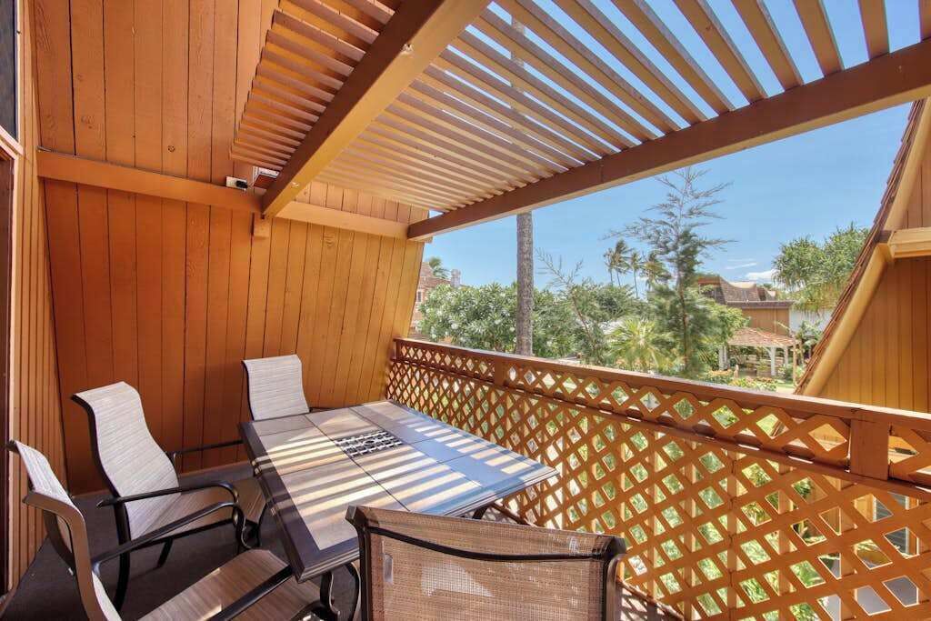 A wooden deck with a table and chairs, a lattice railing, and a view of greenery and buildings.