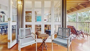 Ein Zimmer mit einem großen Glasfenster, das auf einen Balkon führt, Korbmöbeln und Holzboden.