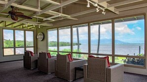 A room with large windows, wicker furniture, and a ceiling fan. - NEW Fall Sale Second-Floor Molokai Condo with Pool, Tennis and Views (Kaunakakai)