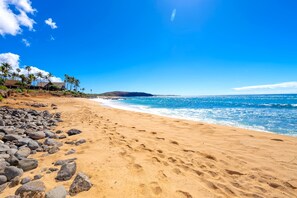 A beach with clear blue water, a sandy shore, and a few palm trees. - New Fall Special Molokai 1BR Corner Condo with Screened Wraparound Lanai (Maunaloa)