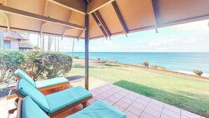 A covered outdoor area with lounge chairs, a view of the ocean, and a grassy lawn.