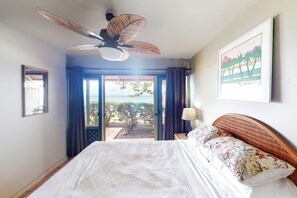 Une chambre avec un lit, un ventilateur de plafond, une vue à travers une porte vitrée et un tableau encadré au mur.