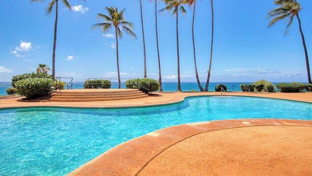 A swimming pool with clear blue water, surrounded by palm trees and a view of the ocean.