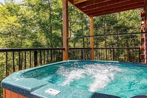 A hot tub on a wooden deck with a view of trees. - Birchwood Lodge (Pigeon Forge)