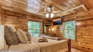 Ein Schlafzimmer einer Holzhütte mit einem Bett, Kissen, einem Nachttisch, einer Lampe und einem Deckenventilator.