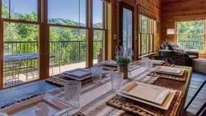 Eine Holzhütte mit großen Fenstern, einem Essbereich mit gedeckten Tischen und einem Balkon mit Blick auf Grünflächen.