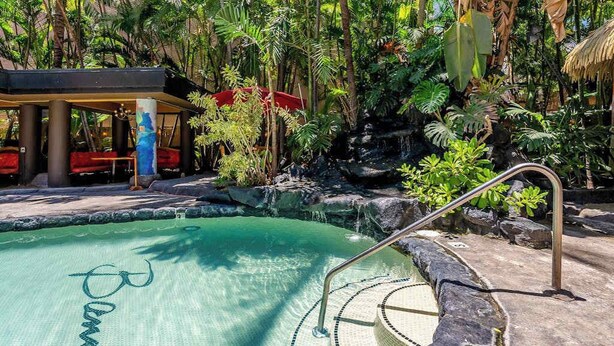 A pool with a waterfall, surrounded by tropical vegetation and a covered seating area. - NEW Fall $pecial Central Waikiki Condo Near Beach and Zoo (Honolulu)