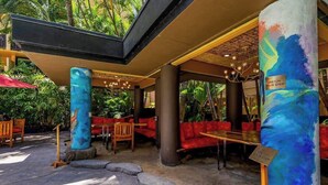 An outdoor seating area with red cushioned benches, a stone pathway, and a tropical garden backdrop. - NEW Fall $pecial Central Waikiki Condo Near Beach and Zoo (Honolulu)
