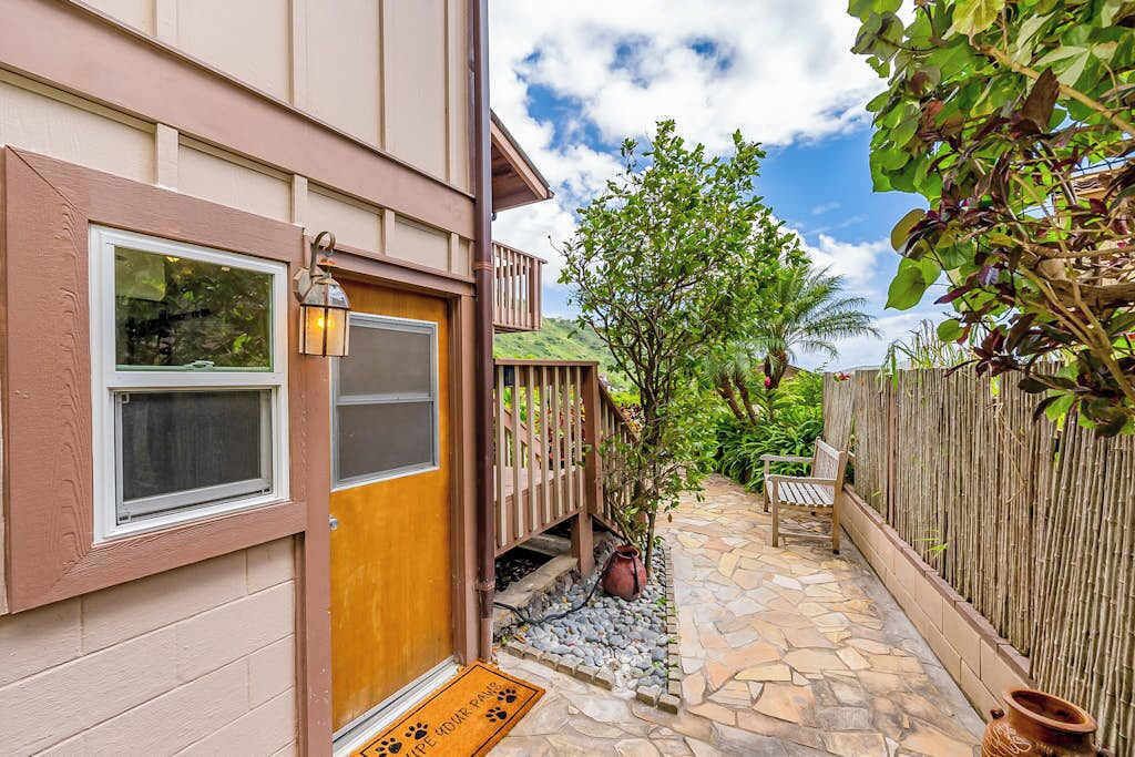 Une maison avec une porte en bois, un chemin de pierres, une clôture en bois et un banc.