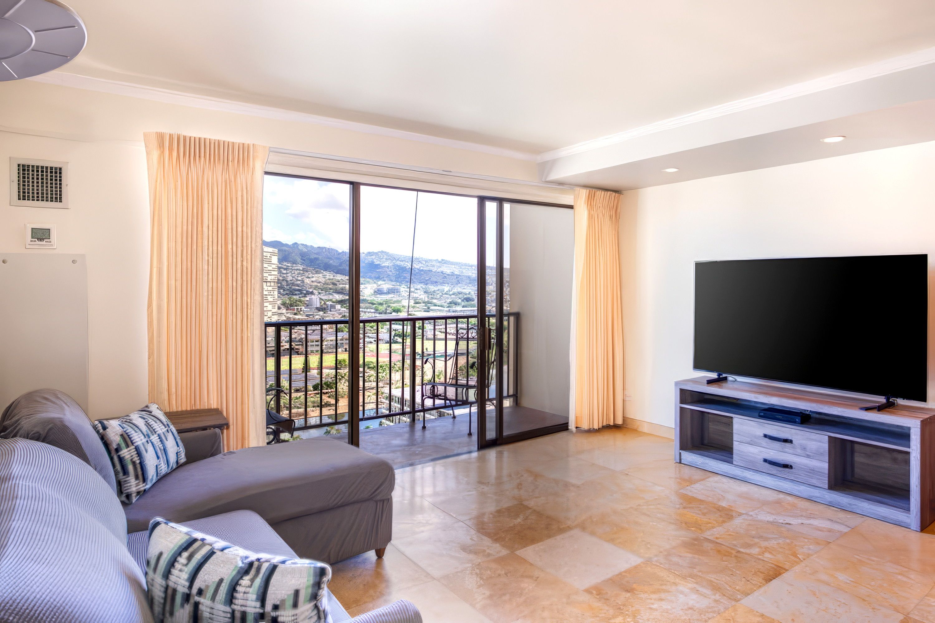 A modern living room with a large TV, a sofa, and a balcony with a city view.
