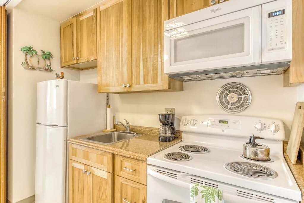 A kitchen with wooden cabinets, a white refrigerator, a microwave, a stove, and a coffee maker.
