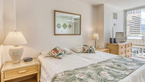 Quarto de hotel com cama, mesa de cabeceira, cômoda, espelho e janela com vista para edifícios.