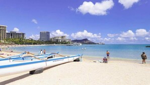 Uma praia com barcos, céu claro e edifícios ao fundo.