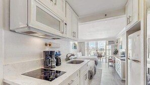 A modern kitchen with white cabinetry, a built-in stove, and a large window offering a view of the city. - *New* 30-Night Waikiki Studio with Lanai and Pool (Honolulu)