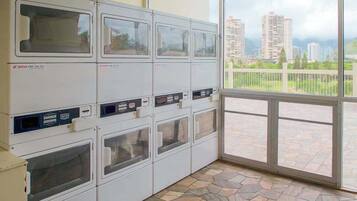 A laundry facility with multiple washing machines, a stone-tiled floor, and a view of a cityscape through a large window.