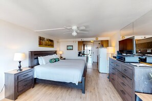 A hotel room with a bed, bedside tables, a desk with a television, and a kitchenette. - NEW Fall $pecial Waikiki Studio with Diamond Head and Ocean Views (Honolulu)