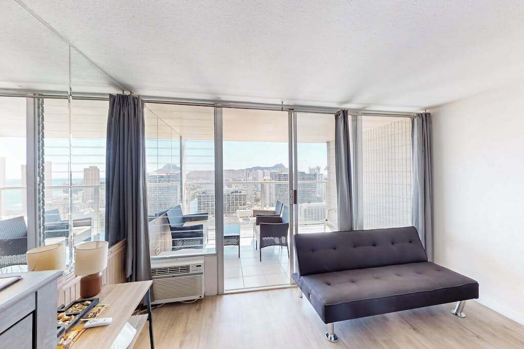 Une chambre d’hôtel moderne, dotée d’un canapé, d’une table à manger et offrant une vue sur le paysage urbain grâce à de grandes fenêtres.